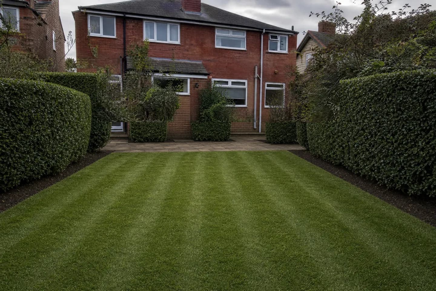 The same garden with a striped mown lawn, squarely trimmed hedges and clean borders after professional maintenance