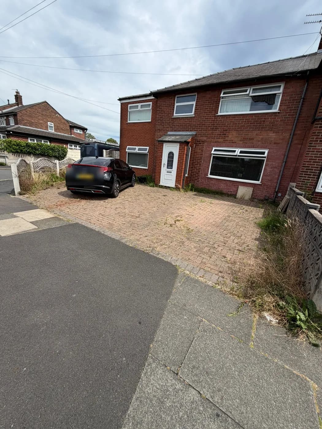 Block-paved driveway before cleaning — weeds and moss through the joints and along the edges