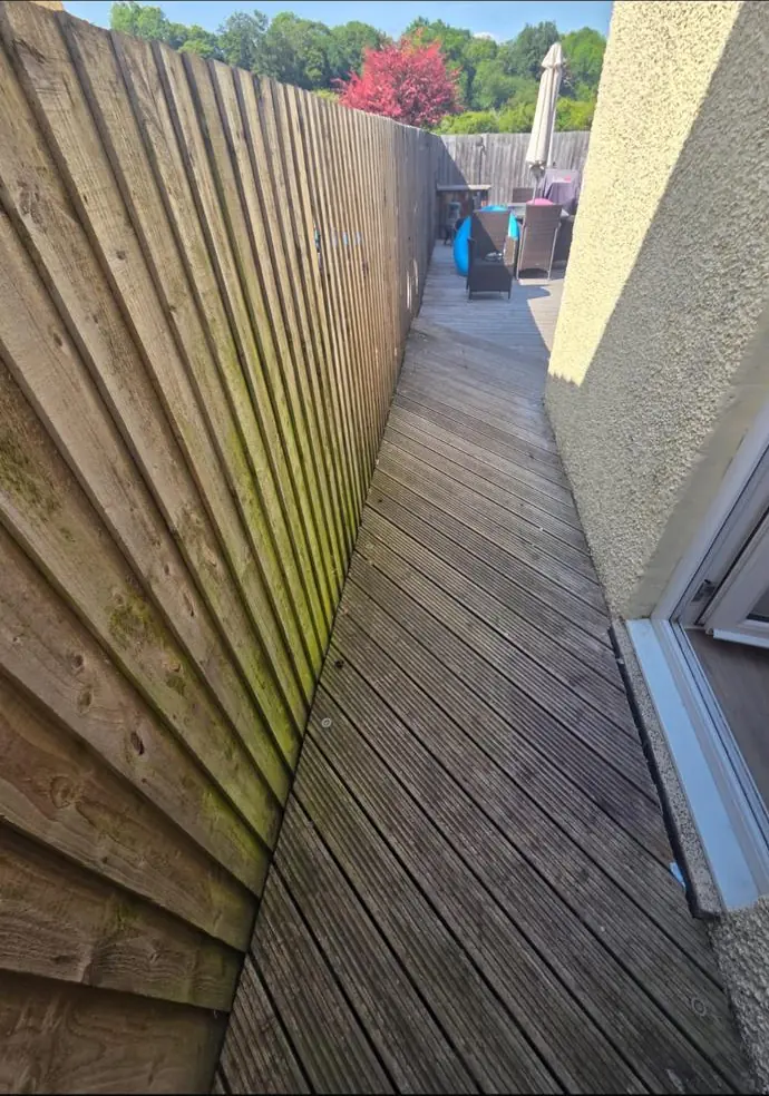 Weathered fence and decking along a narrow side access before restoration