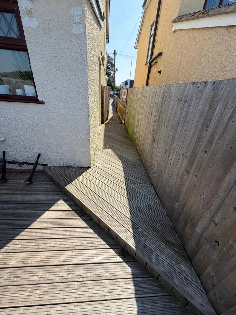 Faded raised decking and fence boards beside the house before preparation