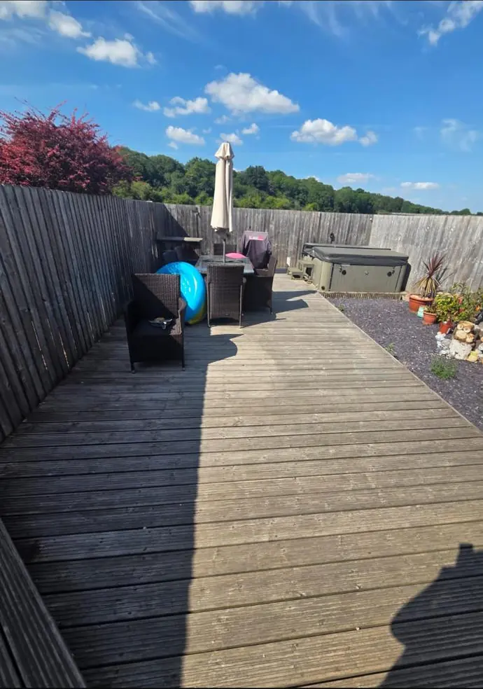Wide view of faded garden fencing and pale weathered decking before treatment