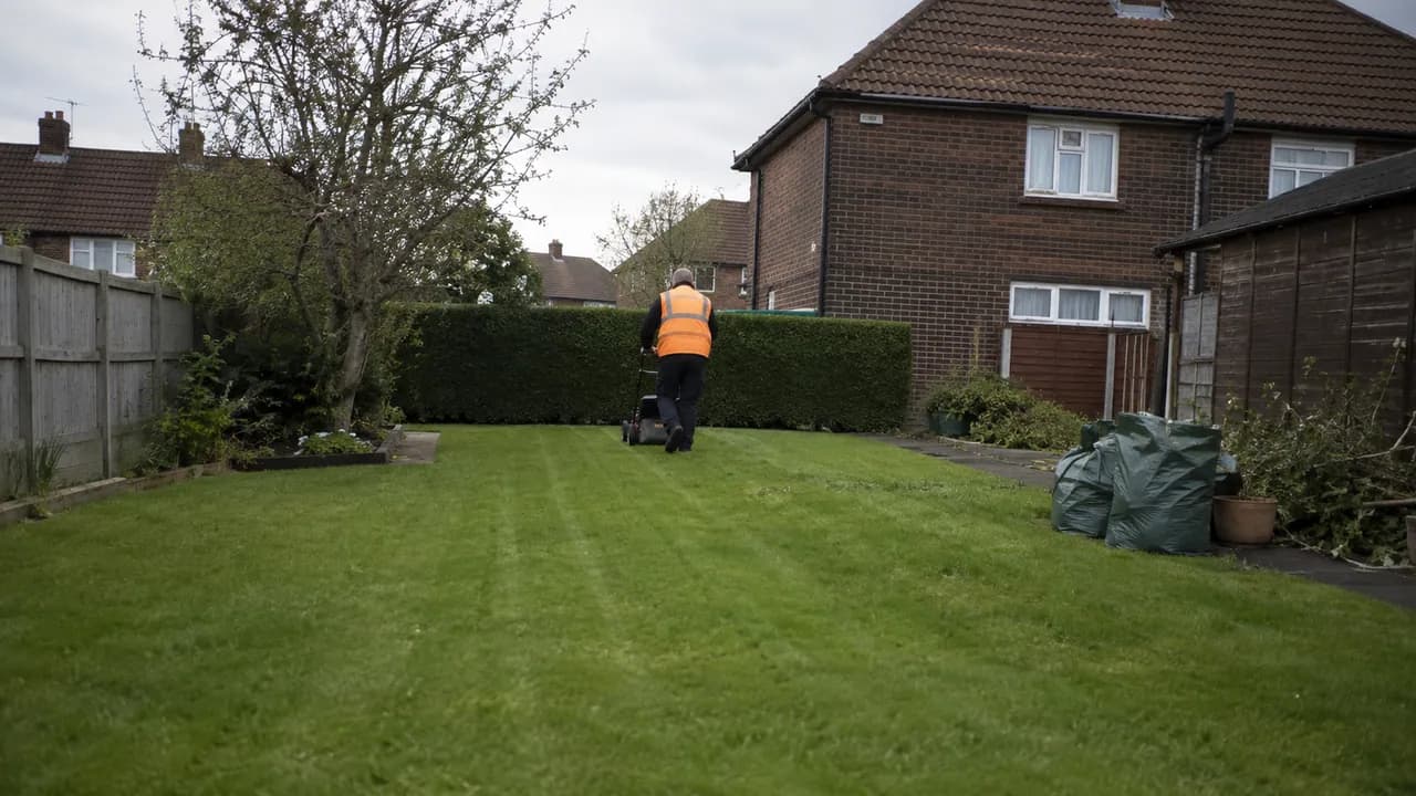 Garden maintenance in progress on a 1950s brick semi-detached house on a flat, open Ellesmere Port estate with a tiled roof