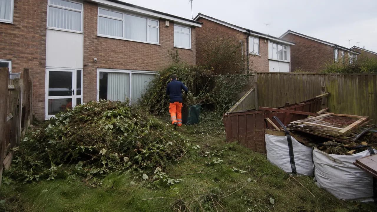 Garden clearance in progress on a 1970s brick townhouse on a new-town estate in Runcorn, Cheshire, open grass verges