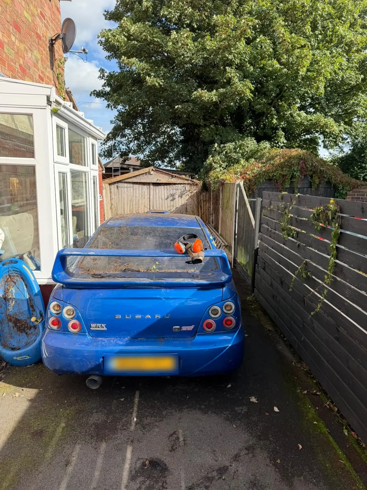 Parked blue car and exposed side-garden ground after brambles and loose cuttings were cleared
