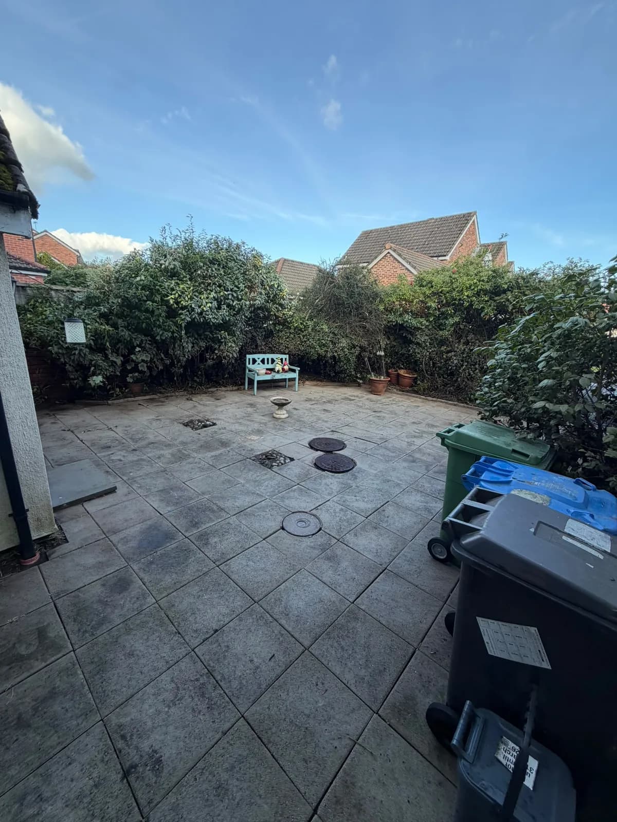 Cleaned garden patio with exposed paving, a blue bench and clear space around the pots